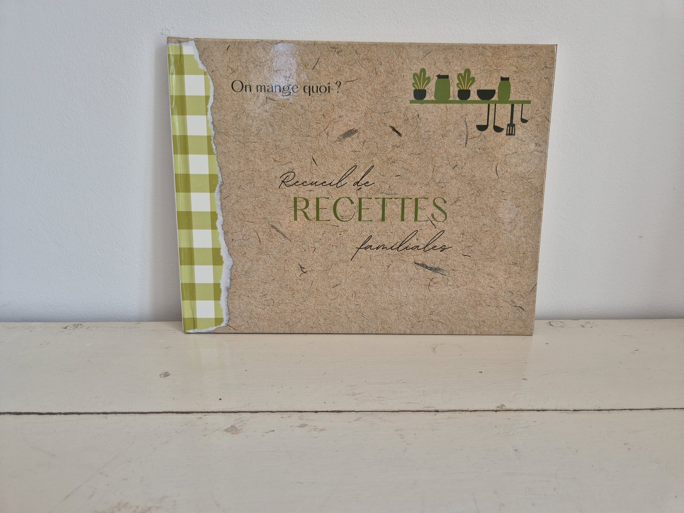 Couverture du livre « Recueil de recettes familiales » posé sur une étagère de cuisine.