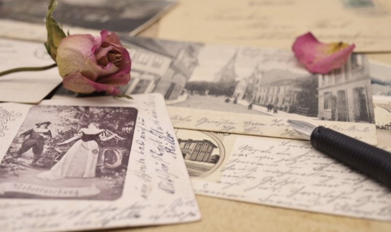 Cartes postales anciennes et lettres manuscrites, rose séchée et stylo plume posés sur du papier sépia.